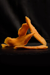 Dried slices of mango fruit on black background.