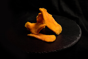 Dried slices of mango fruit on black background.