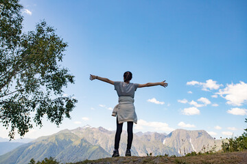 A girl stands on top of a mountain hands up