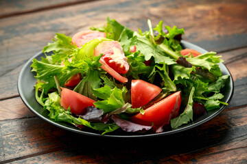 Fresh tomato salad with vegetables on black plate. wooden table. healthy food.