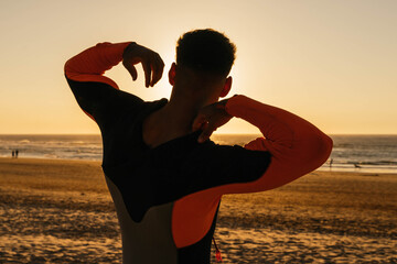 Young surfer putting on the wetsuit before surfing on the beach