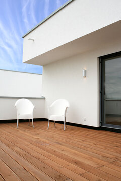 Terrasse oder Balkon mit Holzboden und zwei weißen Stühlen vor weißen Wänden