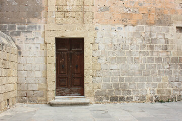 Fototapeta na wymiar Typical Maltese brown wooden old door on the limestone wall. Malta. Concept of traditional Maltese street view, vintage architecture.