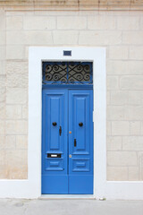 Typical Maltese blue wooden old door on the limestone wall. Malta. Concept of traditional Maltese street view, vintage architecture.