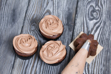 Chocolate cupcakes with cream cheese cream. Next to it is a pastry bag with cream for decoration.