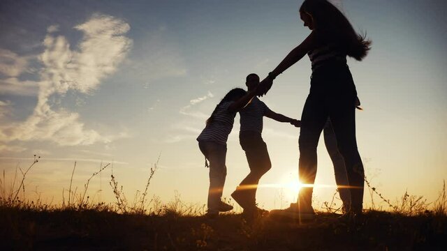 happy family mom dad and daughter play round dance silhouette at sunset. people in park kid dream concept. happy family parents with little kid child daughter play in park on grass holding fun hands