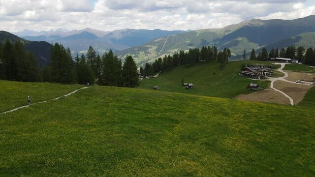 4k video shooting with drone of mountain panoramas, on the italian dolomites alps. snow-capped peaks, green meadows and ski slopes, mountain trails with small wooden houses. blue skies with clouds.