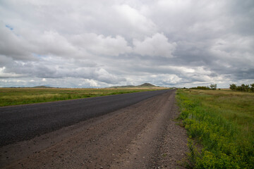 Fototapeta premium View of the track in a field with hills and dark clouds.