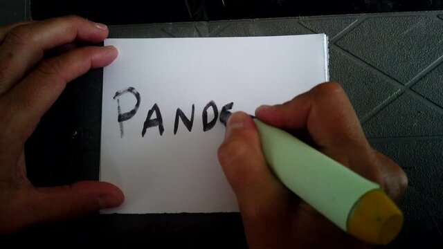 Adult Caucasian female writes with black magic marker and scribes in block capital letters the word pandemic on white piece of square paper, covid-19 shutdown and quarantine, directly above static
