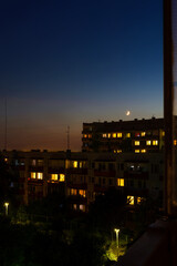 Fototapeta premium Waxing crescent moon rising over apartment blocks at nightfall, urban view, cityscape