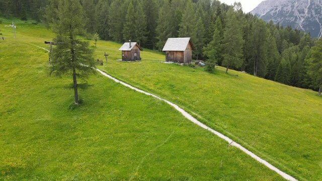 4k video shooting with drone of mountain panoramas, on the italian dolomites alps. snow-capped peaks, green meadows and ski slopes, mountain trails with small wooden houses. blue skies with clouds.