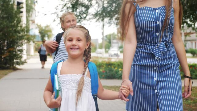 mom and daughter go to school. happy family school education concept. schoolgirl with mom go hand in hand to school on footpath in the park. little girl with a briefcase lifestyle time to study
