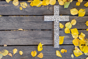 White wooden cross with the Lord's Prayer on a shabby dark wooden board with yellow leaves background