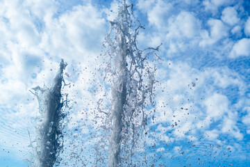 Two jets of fountain with water bubbles on a cloudy sky background