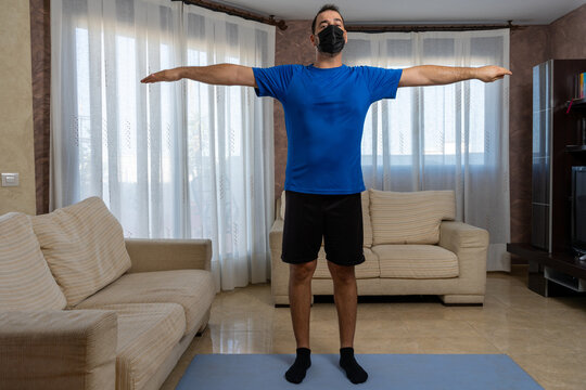Low-bearded man exercising with black and blue sportswear and mask to prevent coronavirus