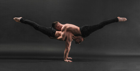 two twin brothers in black jeans with a naked torso perform acrobatic elements, black background
