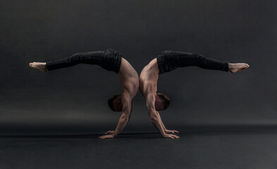 two twin brothers in black jeans with a naked torso perform acrobatic elements, black background
