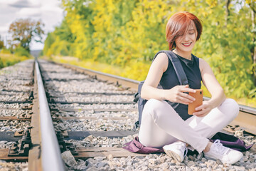 portrait cute young girl sitting on railway tracks with phone in hands