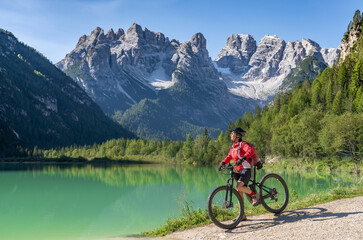 nice and active senior woman riding her electric mountain bike at Duerrenstein Lake in the Hoehlenstein valley between Toblach and Cortina Dampezzo, Three Peaks Dolomites, South Tirol, Italy
