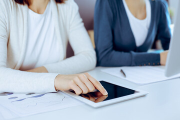 Businesswoman pointing at tablet computer screen while giving presentation to her female colleague. Group of business people working at the desk in office. Teamwork concept