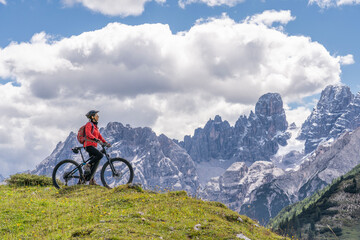 Fototapeta na wymiar nice and active senior woman riding her electric mountain bike on the high plateau of Pratto Piazzo in the three peaks Dolomites , rocky silhouette of Mount Cristallo in background, South Tirol, Italy