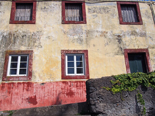 Fototapeta na wymiar facade of a typical old spanish house painted in faded yellow and red colors surrounded by a grey wall with plants in Funchal, Tenerife
