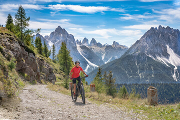 Fototapeta na wymiar nice and active senior woman riding her electric mountain bike on a old military road from Toblach upt to the summit of Marchkinkele eith spectacular view to the Three peaks of Lavaredo, South Tirol, 