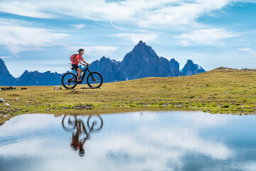 nice woman riding her electric mountain bike the Three Peaks Dolomites, reflecting herself in the...