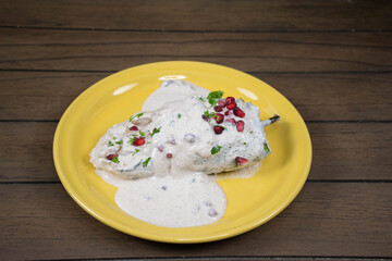 Typical Mexican dish, Chiles en nogada on a yellow plate on wooden background