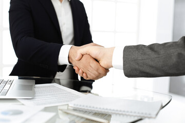 Unknown diverse business people are shaking hands finishing up meeting at the desk in office, close-up. Handshake concept