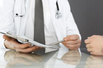 Unknown male doctor and woman-patient discussing current health examination while sitting in clinic...