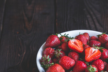 Fresh strawberries in a white bowl on wooden table with low key scene. copy space