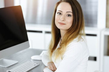 Business woman headshot in sunny office. Unknown businesswoman sitting behind computer monitor