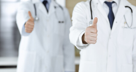 Group of modern doctors standing as a team with thumbs up or Ok sign in hospital office, close-up. Medical help, insurance in health care and medicine concept