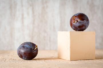 Creative still life. Ripe blue plum on a beige cube and one plum on the table. The importance of vitamins