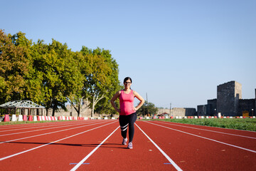 Active, 6 months pregnant woman workingout on track field on sunny morning. Attractive female doing walking lunges toward the camera.