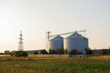 Fototapeta na wymiar Steel grain elevator stands in the field. Agriculture business. Cereals storage. Copy space. Harvesting seeds