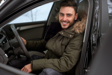 Young attractive Caucasian man sits at the wheel of his car sunny winter day.