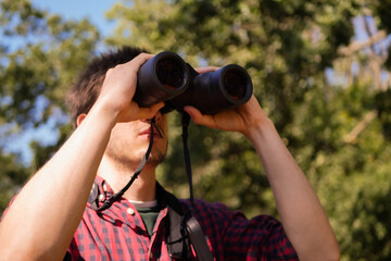 Man in plaid short look through binoculars. Forest hiking. Bird watching. Searching for...