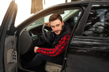 Young attractive Caucasian man sits at the wheel of his car sunny winter day.