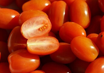 Date or cocktail tomatoes close up as a background. One of the fruits is cut in halves. 