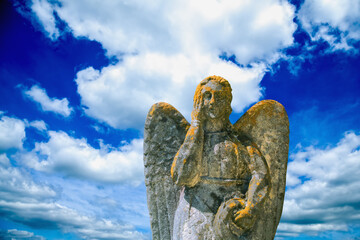Beautiful angel. Fragment of an antcient stone statue in moss against blue sky.