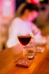 A lifestyle atmospheric photo of a cocktail in a nick and nora glass at the bar in the evening, people in the background, high iso, selective focus