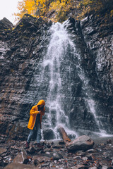 woman in yellow raincoat at autumn waterfall