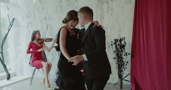 Adult couple of dancers performs ballroom dance to accompaniment of the violin