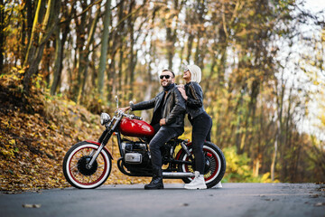Fototapeta na wymiar Pretty couple near red motorcycle on the road in the forest with colorful blured background