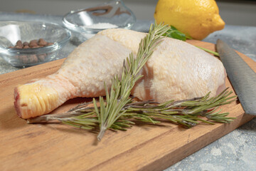 Raw chicken leg on wooden board with rosemary branch, mushrooms, salt and pepper.