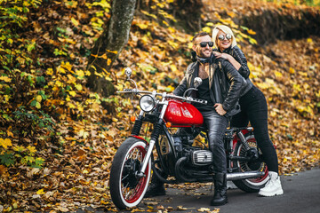 Plakat Pretty couple near red motorcycle on the road in the forest with colorful blured background