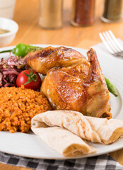Portion of grilled chicken served with bulgur pilaf, onion and tomatoes on wooden table