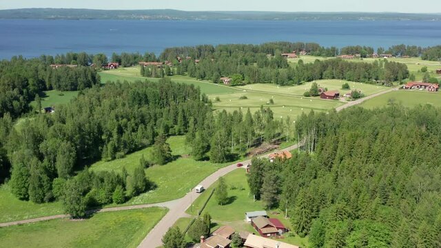Swedish countryside with red wooden houses and summer fields. Blue clean lake and farms in aerial drone shot. Single car and motorhome caravan driving on small country road. Sweden dream on sunny day